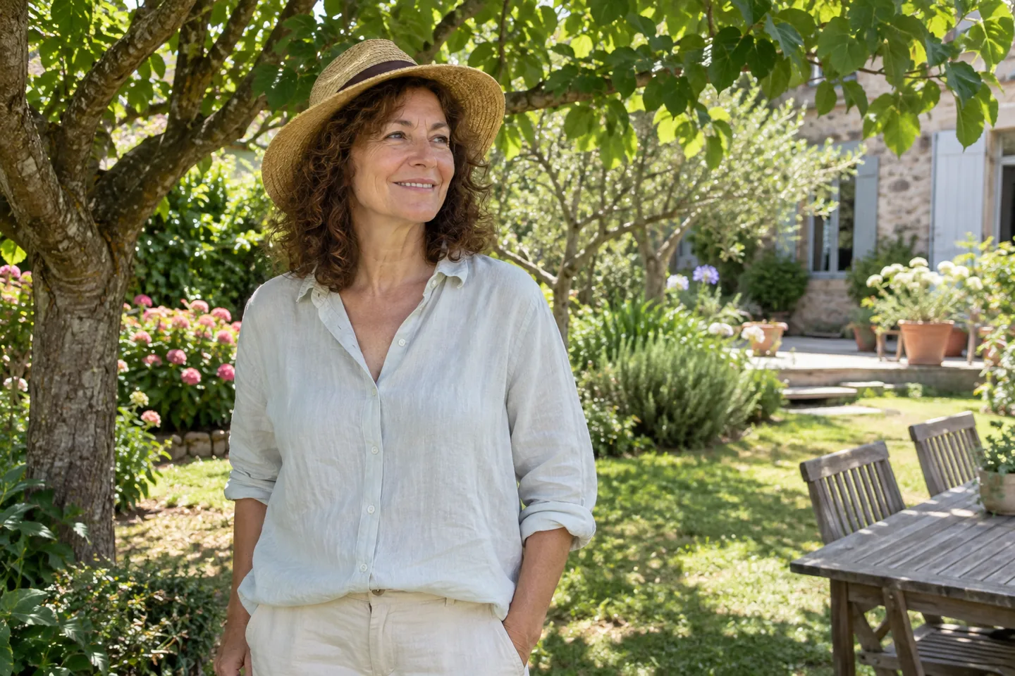 Femme portant manches longues et chapeau à l’ombre d’un arbre dans un jardin.