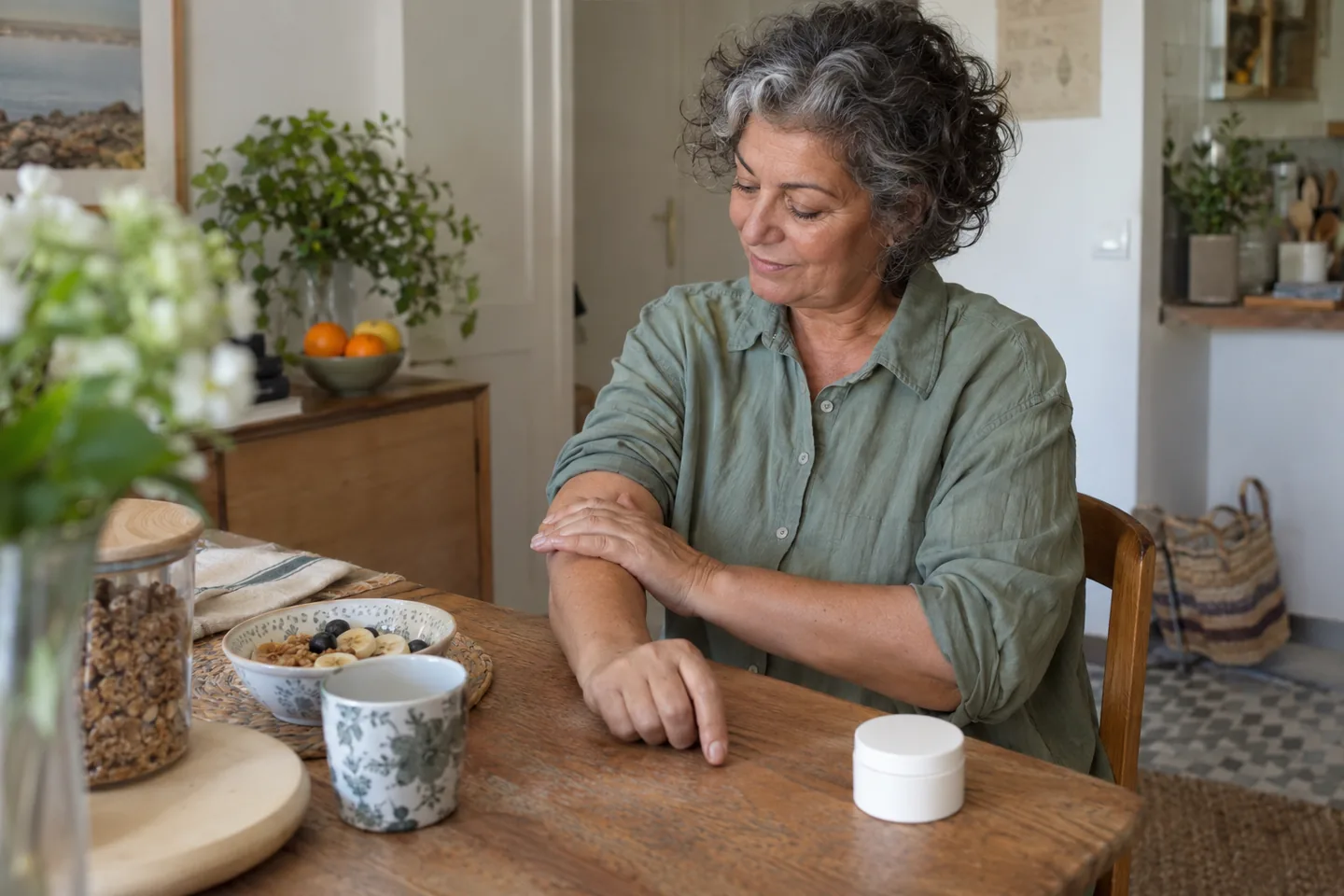 Femme en chemise claire observant son avant-bras près d’une fenêtre