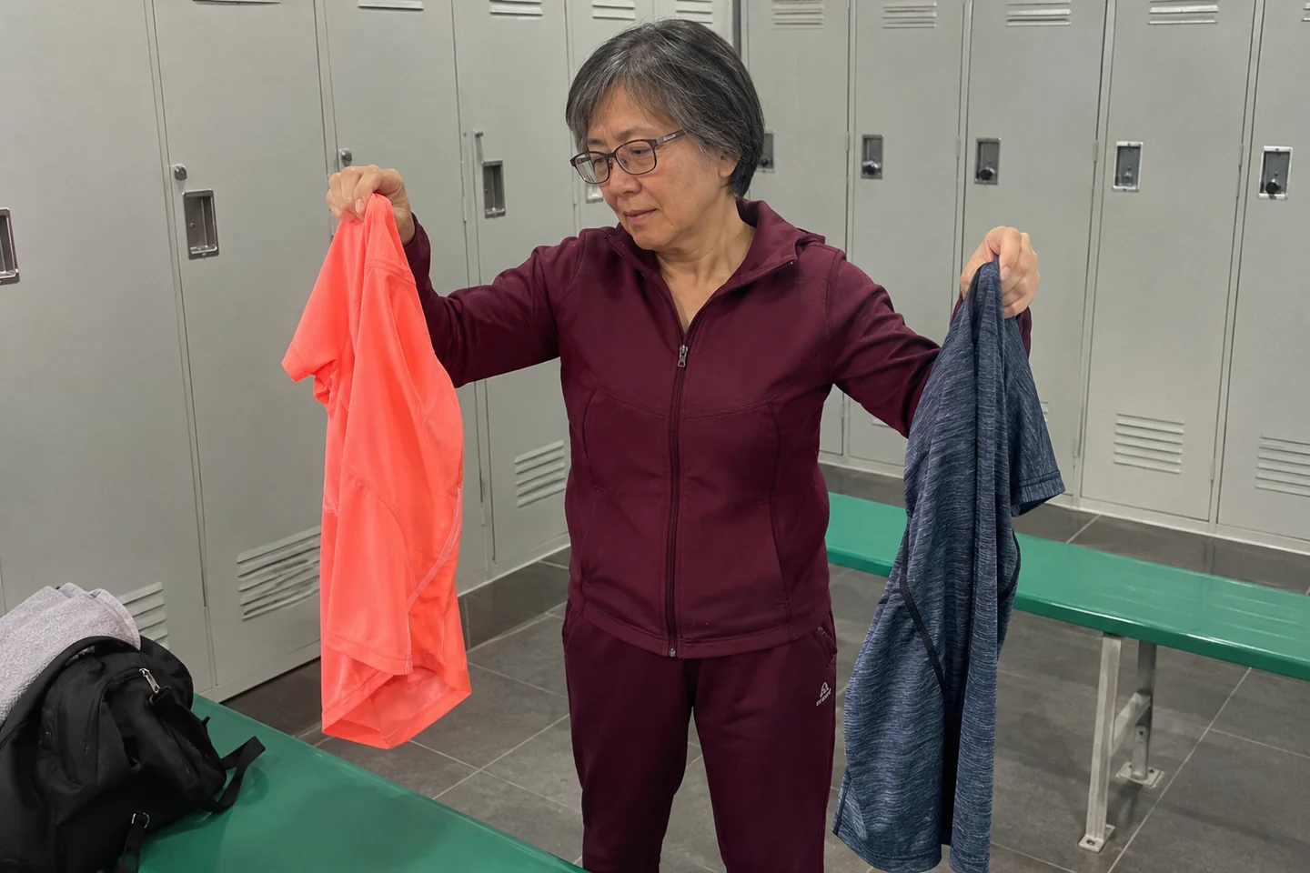 Une femme compare deux hauts de sport dans un vestiaire